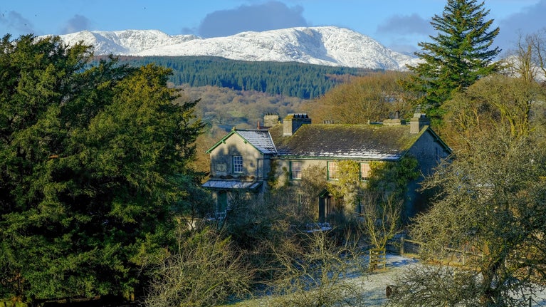 A view of Hill Top House and farm, Cumbria, on a clear winter's day with snow on the backdrop fells